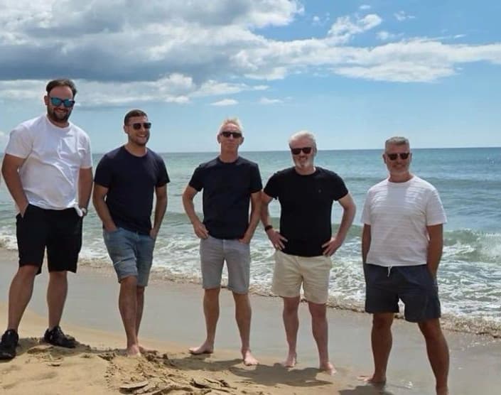 Five members of the Quay Group team standing on the shoreline at Bournemouth beach