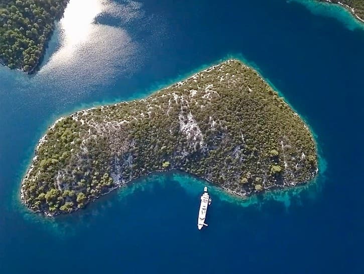 Yacht anchored off a small wooded island, seen from the air