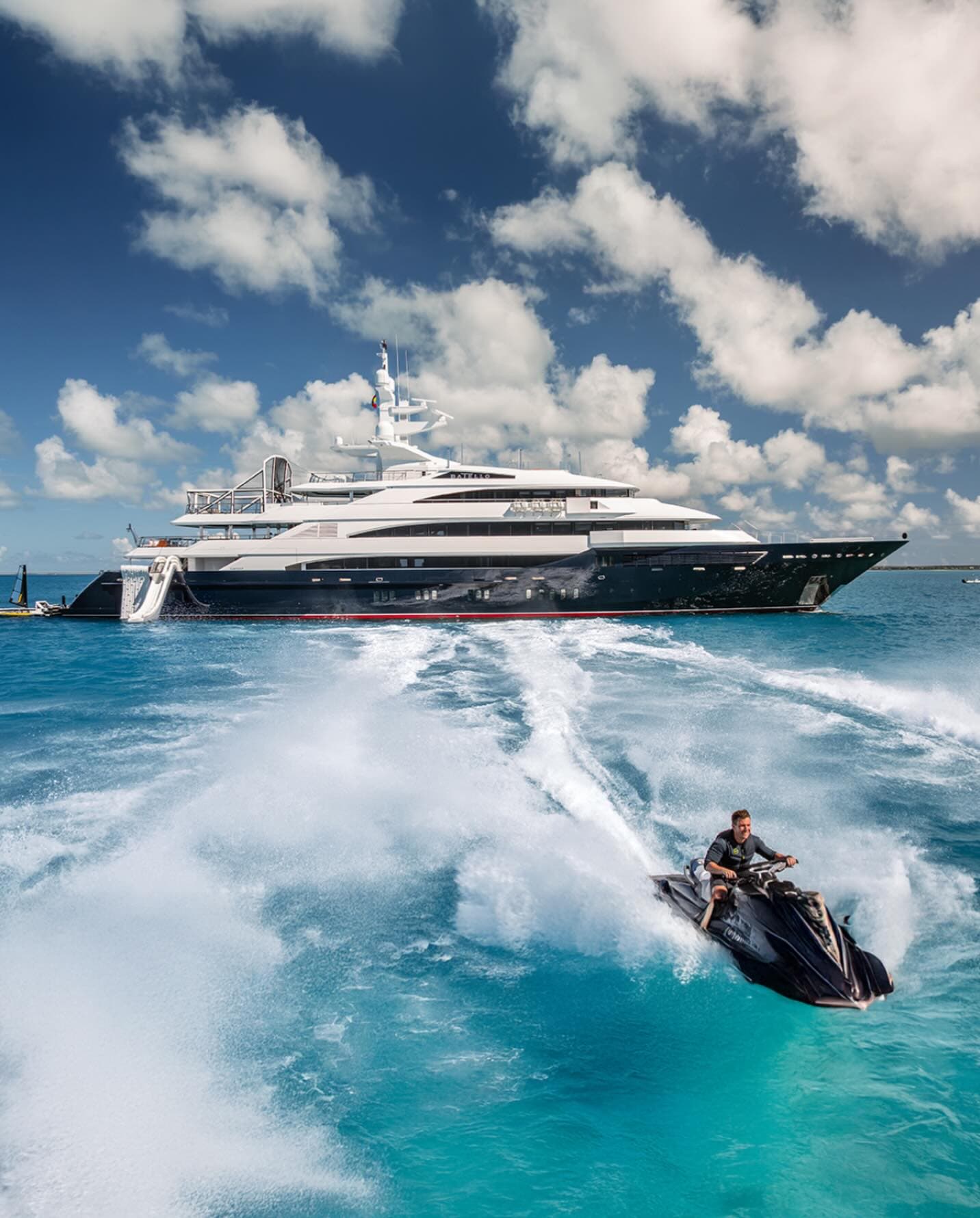 Jetski running alongside a dark-hulled superyacht at speed