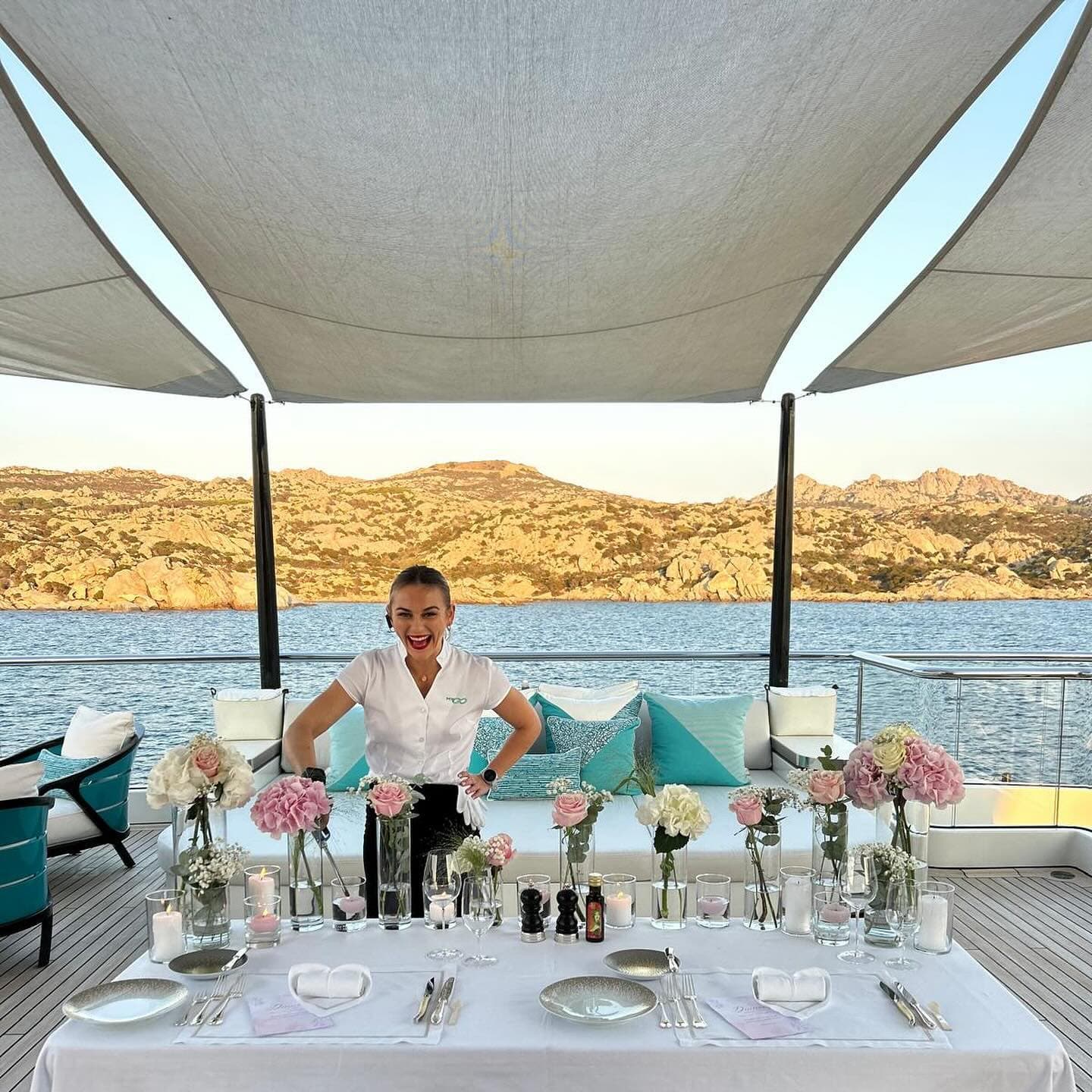 Stewardess behind a table she has dressed for dinner, Sardinian coast behind