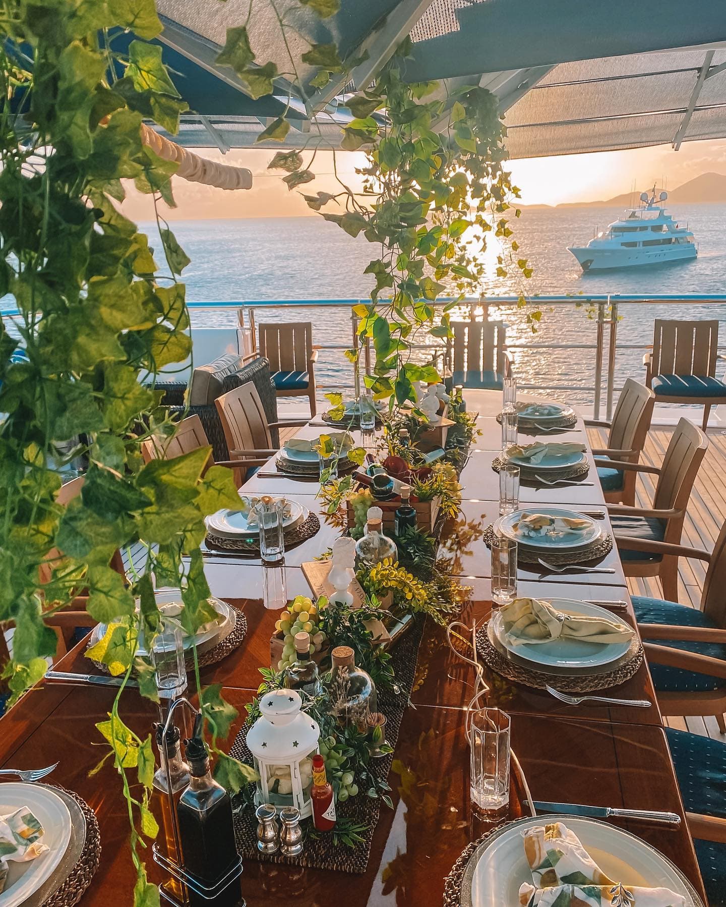 Long table laid for dinner on the aft deck as the sun drops, a second yacht at anchor beyond