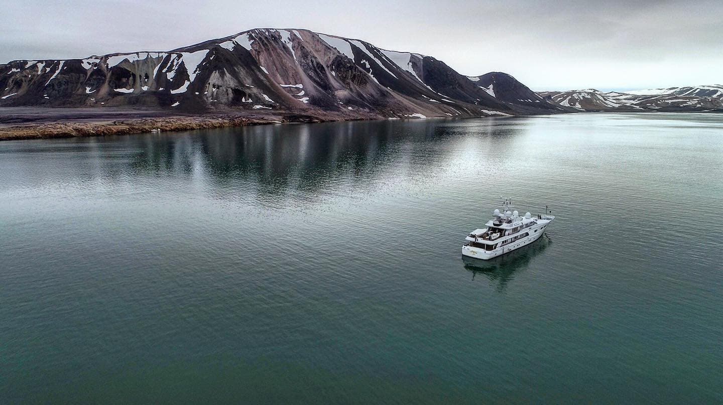 Expedition yacht at anchor in an Arctic fjord below snow-streaked mountains