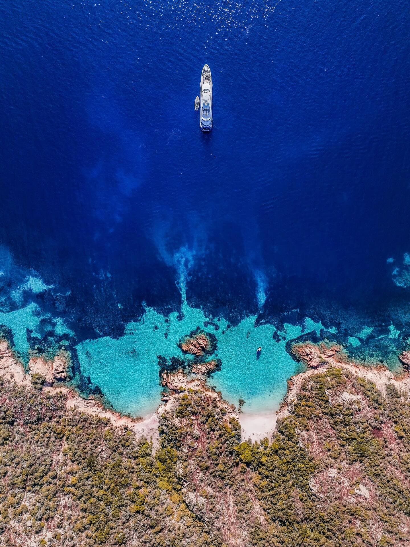 Superyacht at anchor above a turquoise cove, shot from directly overhead