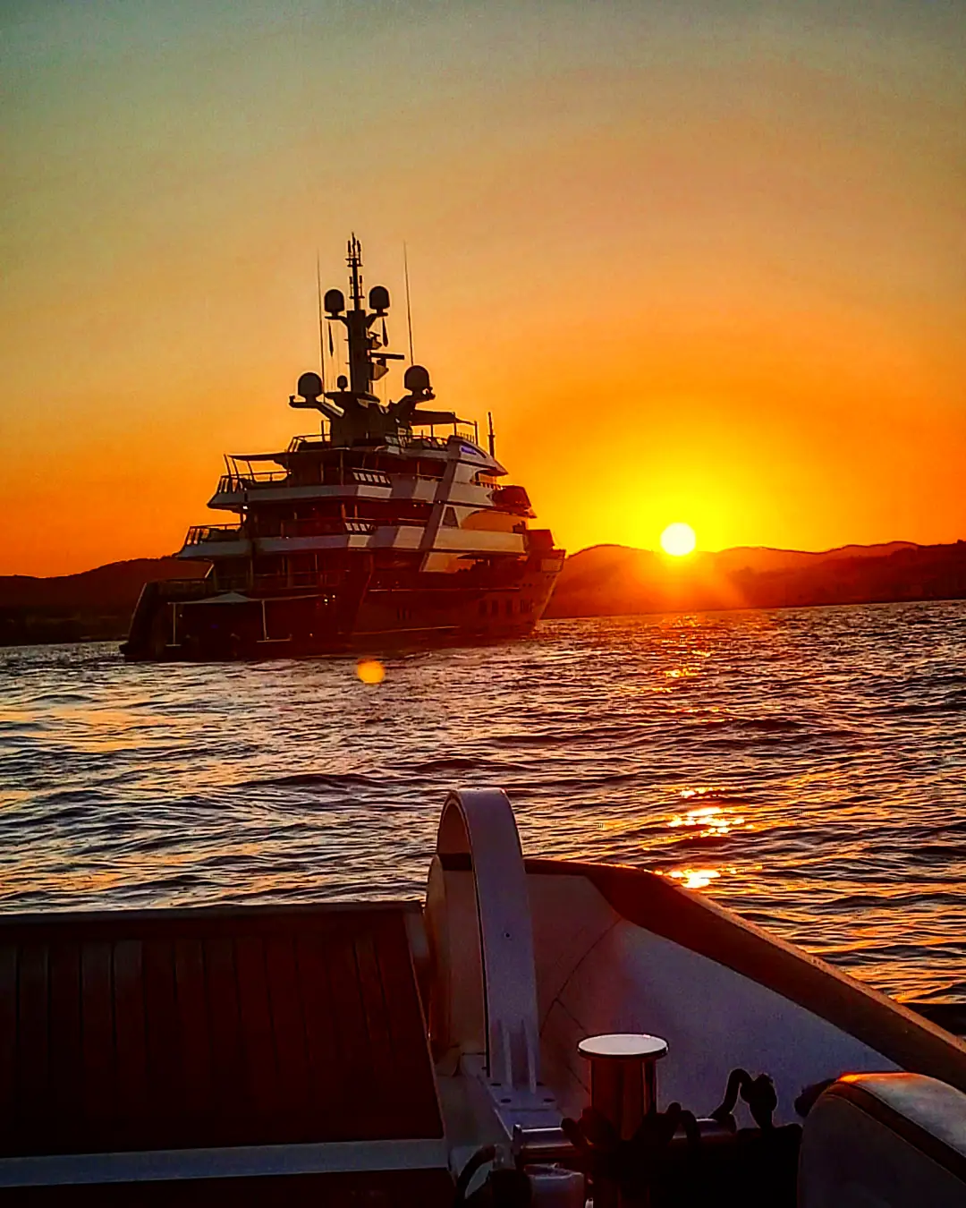 Superyacht silhouetted against the sunset, seen from the tender running back