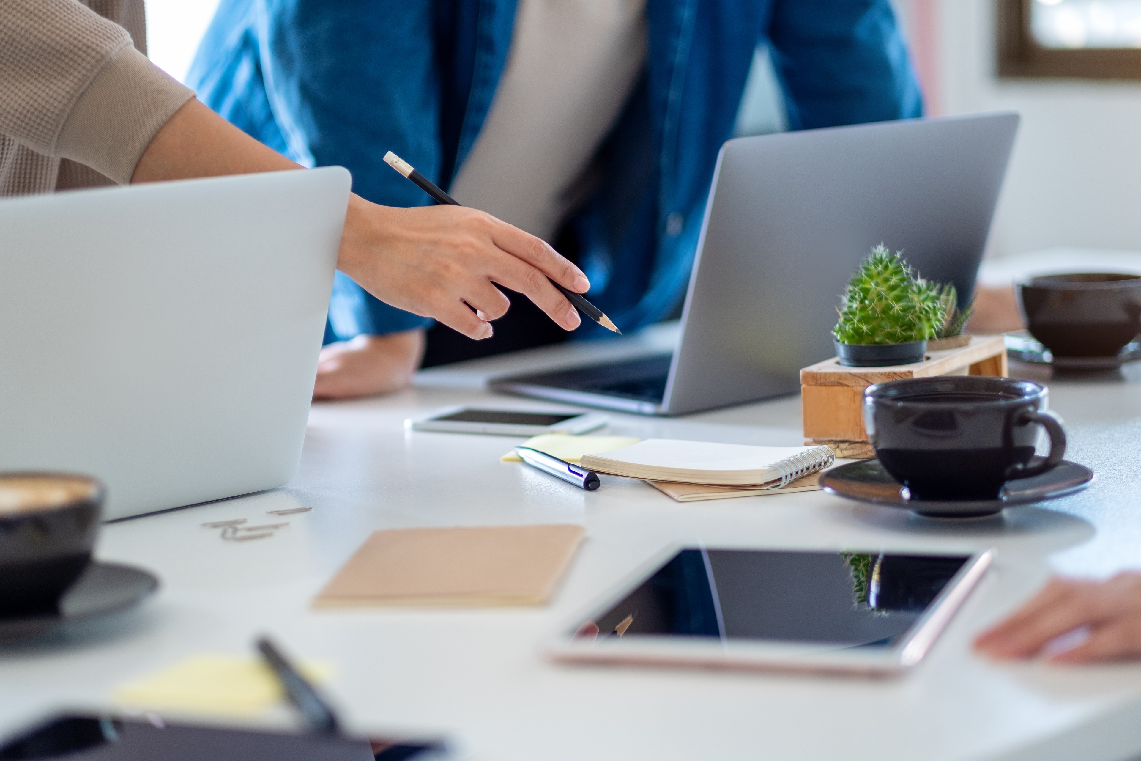 Colleagues at a desk with laptops, one pointing with a pencil during a discussion