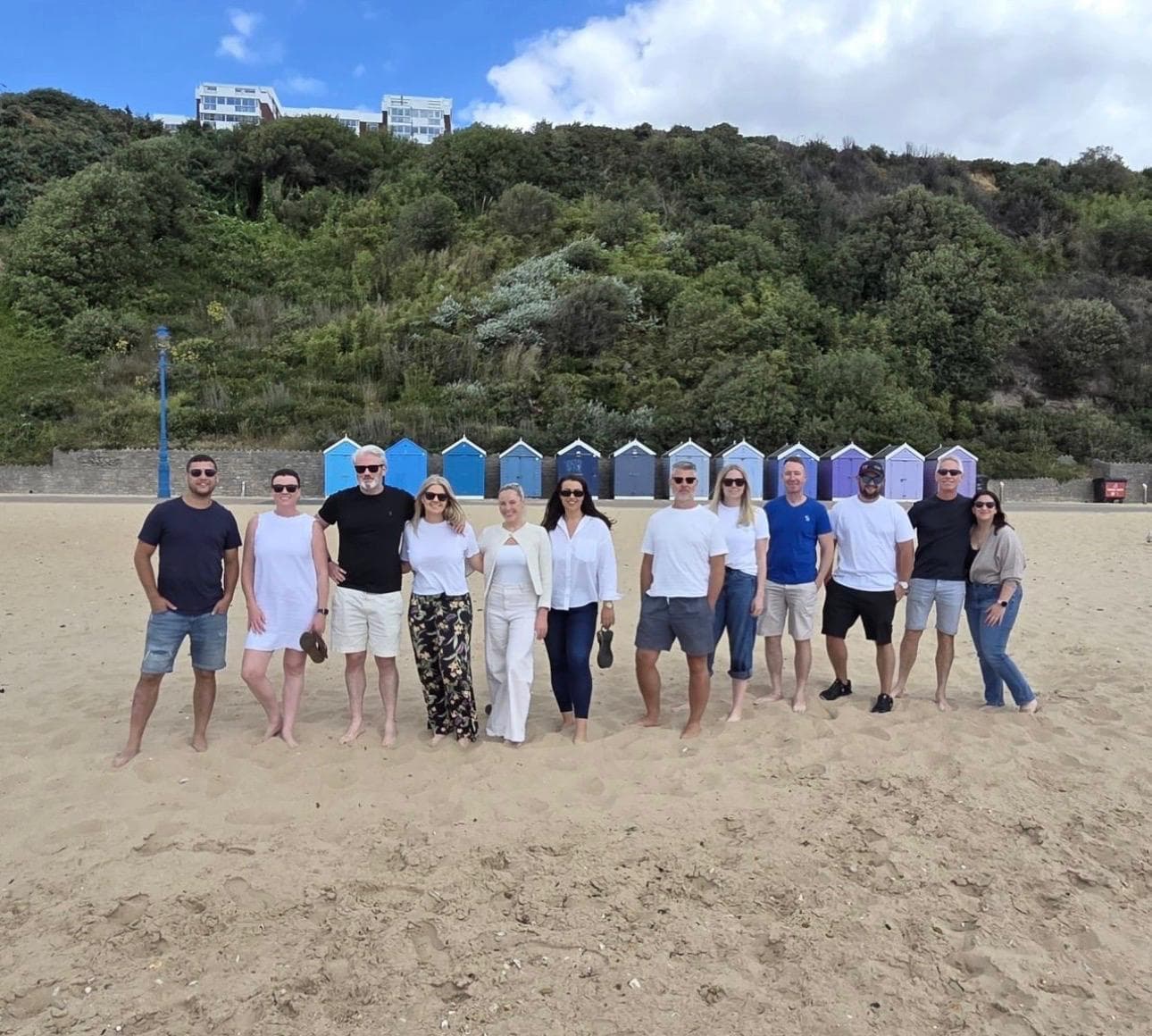 The Quay Group team on the sand in front of a row of blue beach huts in Bournemouth